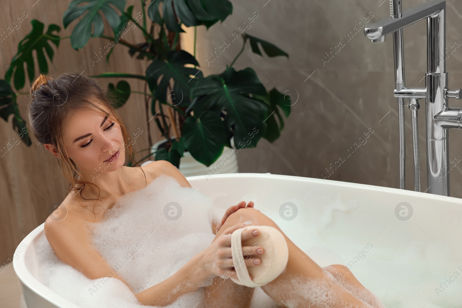 Photo of Beautiful woman with sponge taking bath indoors, space for text