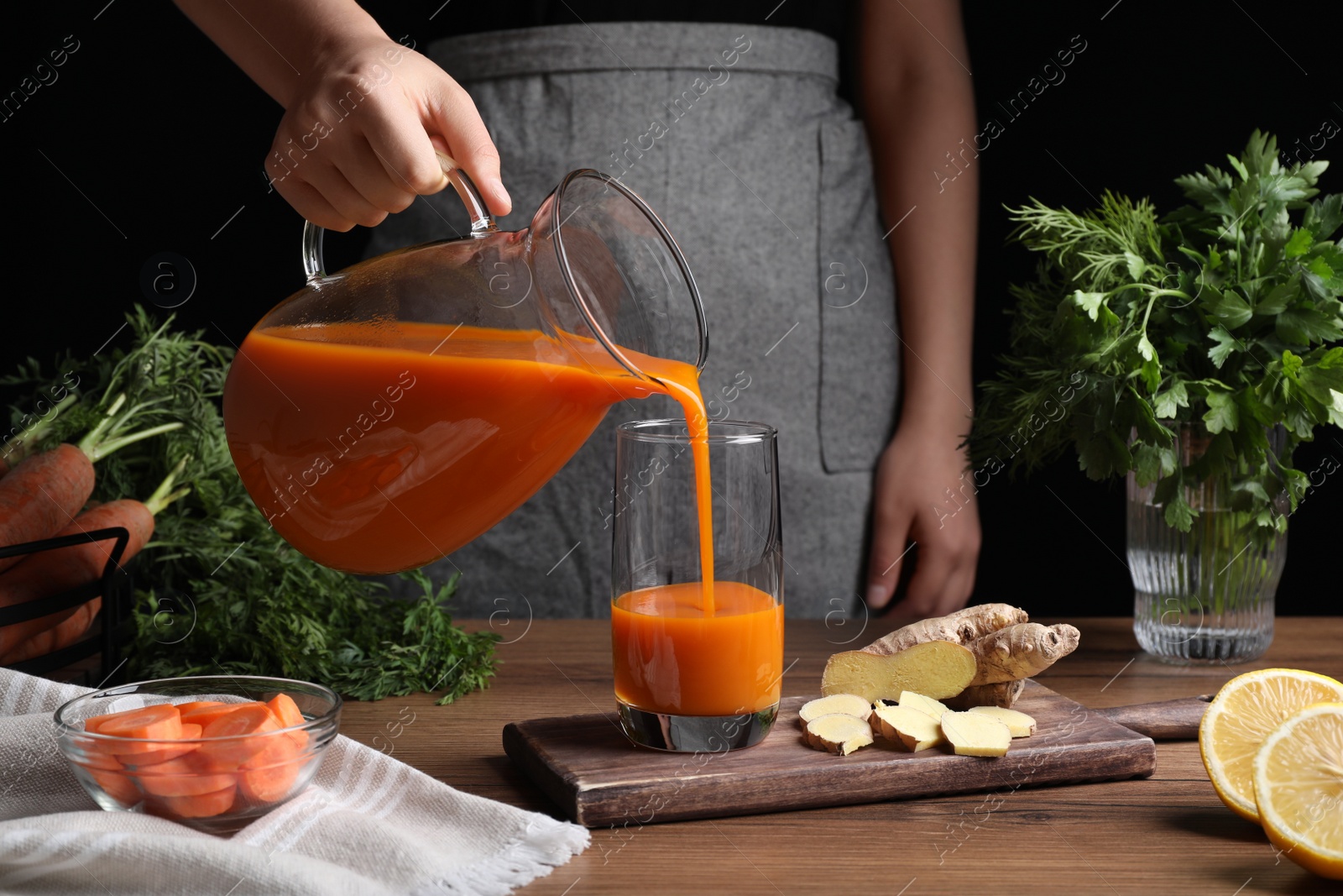 Photo of Woman pouring carrot juice from jug into glass at wooden table, closeup