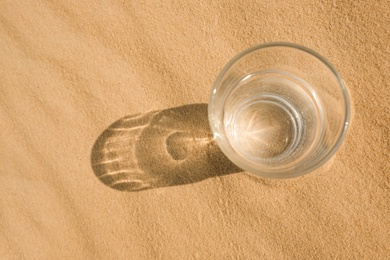 Glass of water on sand in desert, top view. Space for text