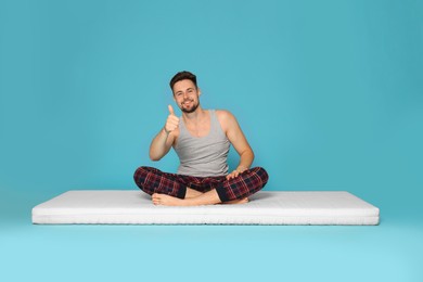 Photo of Smiling man sitting on soft mattress and showing thumb up against light blue background