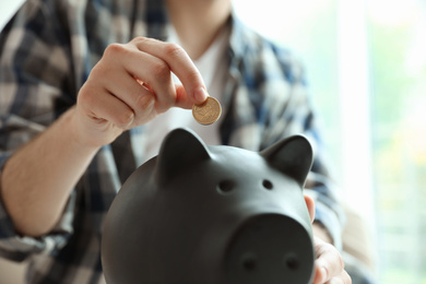 Photo of Man putting coin into piggy bank against blurred background, closeup