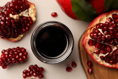 Photo of Glass jar of tasty pomegranate sauce and fresh ripe fruits on white background, flat lay