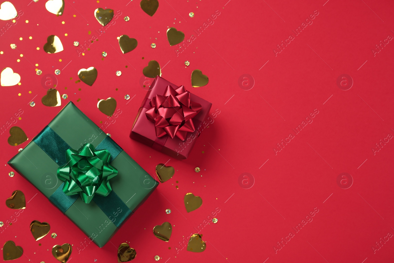 Photo of Gift boxes and shiny confetti on red background, flat lay. Space for text