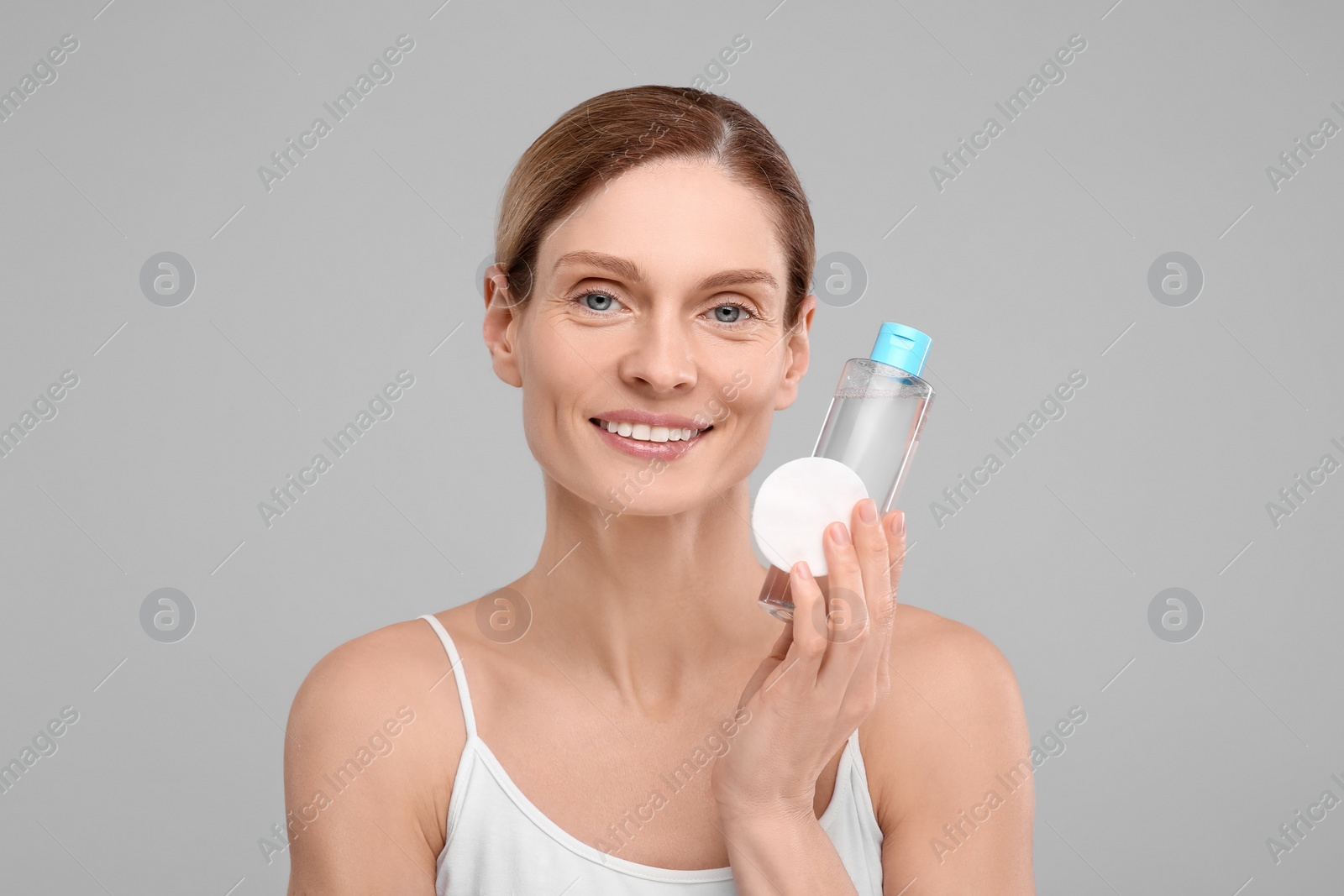 Photo of Beautiful woman with makeup remover and cotton pad on gray background