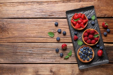 Photo of Tartlets with different fresh berries on wooden table, flat lay and space for text. Delicious dessert