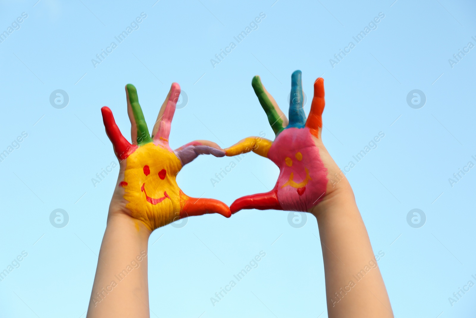 Photo of Kid with smiling face drawn on palms against blue sky, closeup