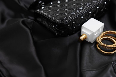 Leather bag, bottle of perfume and golden bracelets on black fabric, closeup. Space for text