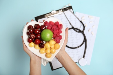 Photo of Female doctor holding plate with fresh fruits over color background, top view. Cardiac diet