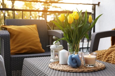 Photo of Soft pillow, blanket, burning candles and yellow tulips on rattan garden furniture outdoors