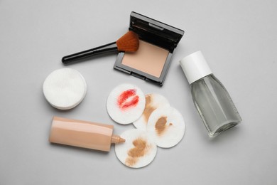 Bottle of makeup remover, different cosmetic products, clean and dirty cotton pads on light grey background, flat lay