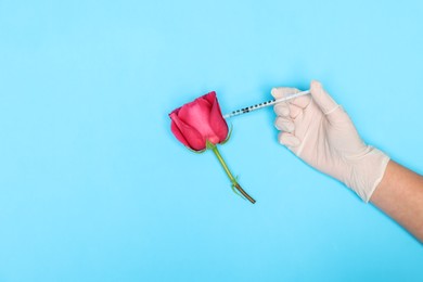 Doctor making injection to rose on light blue background, top view