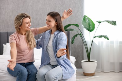 Happy young women sitting on bed at home, space for text