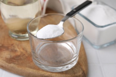 Photo of Baking soda in spoon, glass bowl and vinegar on white table, closeup