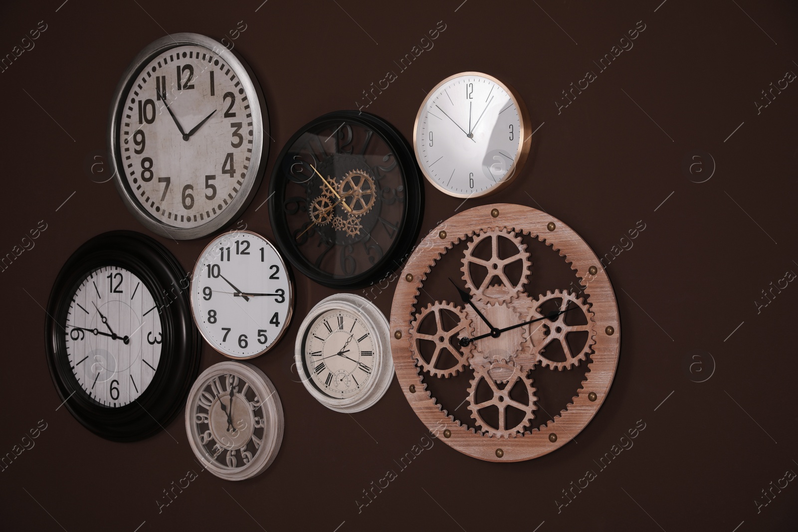 Photo of Collection of stylish clocks on brown wall