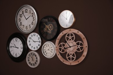 Photo of Collection of stylish clocks on brown wall