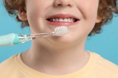 Photo of Cute little boy brushing his teeth with electric toothbrush on light blue background, closeup
