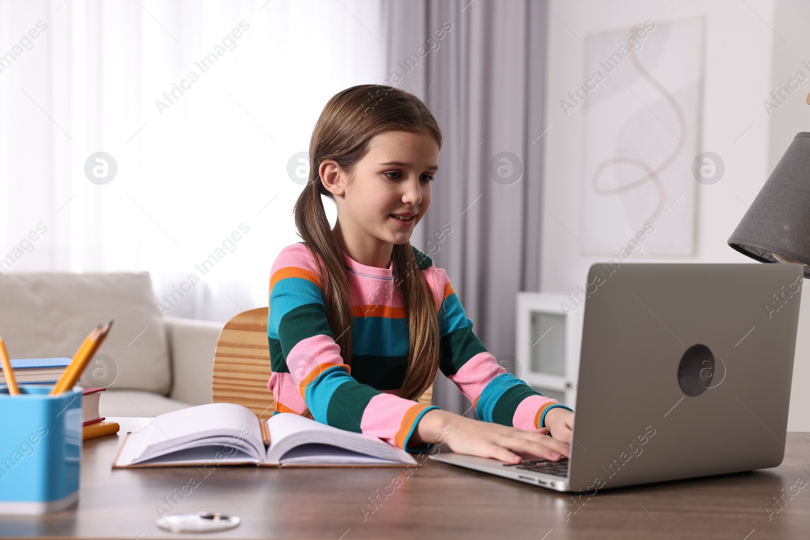 Photo of E-learning. Cute girl using laptop during online lesson at table indoors