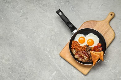 Photo of Frying pan with cooked traditional English breakfast on grey marble table, top view. Space for text