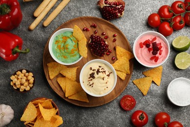Photo of Different kinds of tasty hummus served with nachos on grey table, flat lay