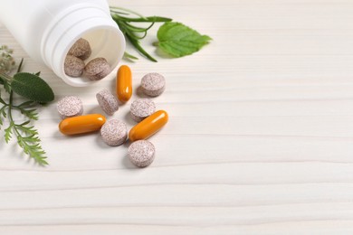 Photo of Different pills and herbs on white wooden table, closeup with space for text. Dietary supplements