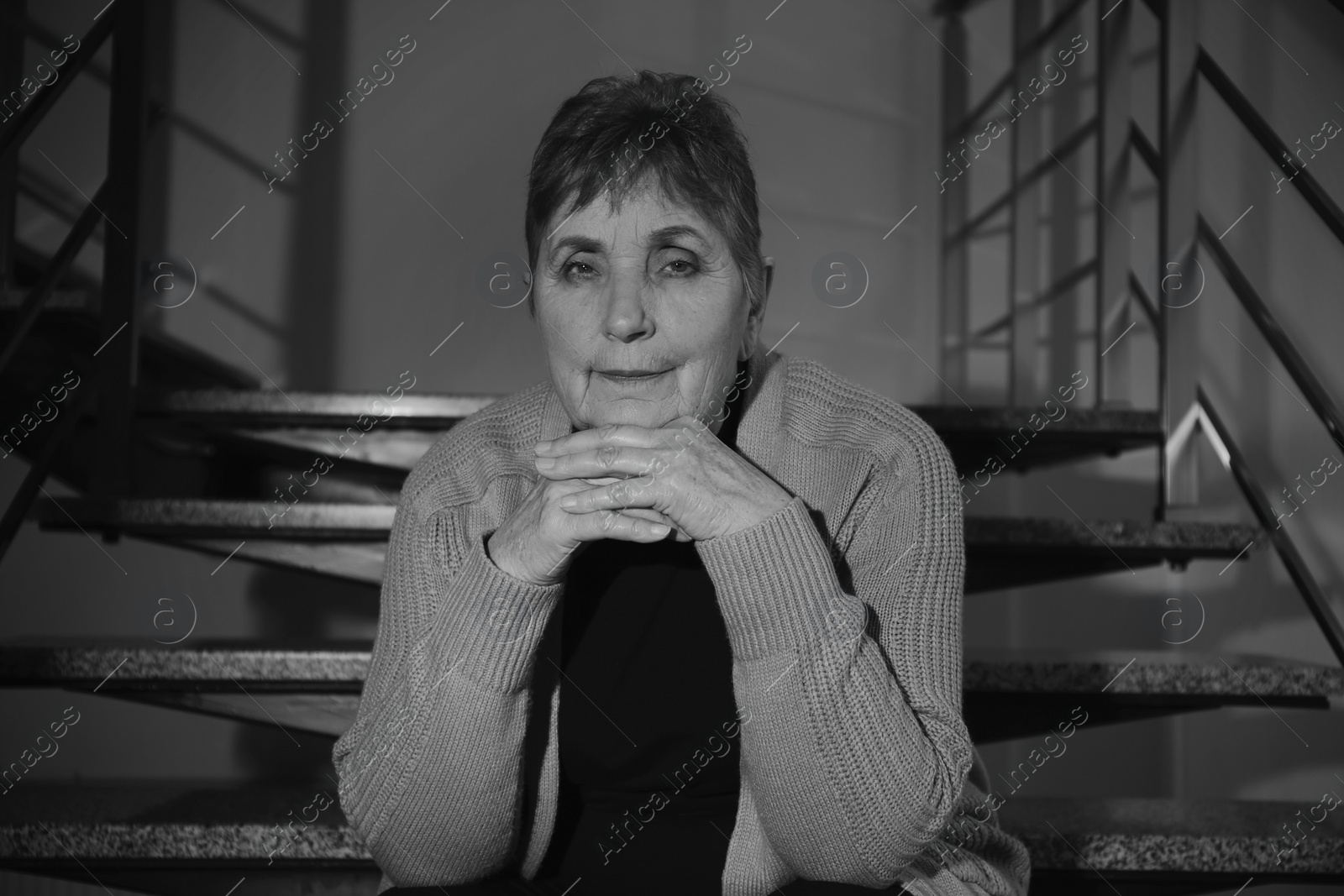 Photo of Poor senior woman sitting on stairs indoors. Black and white effect