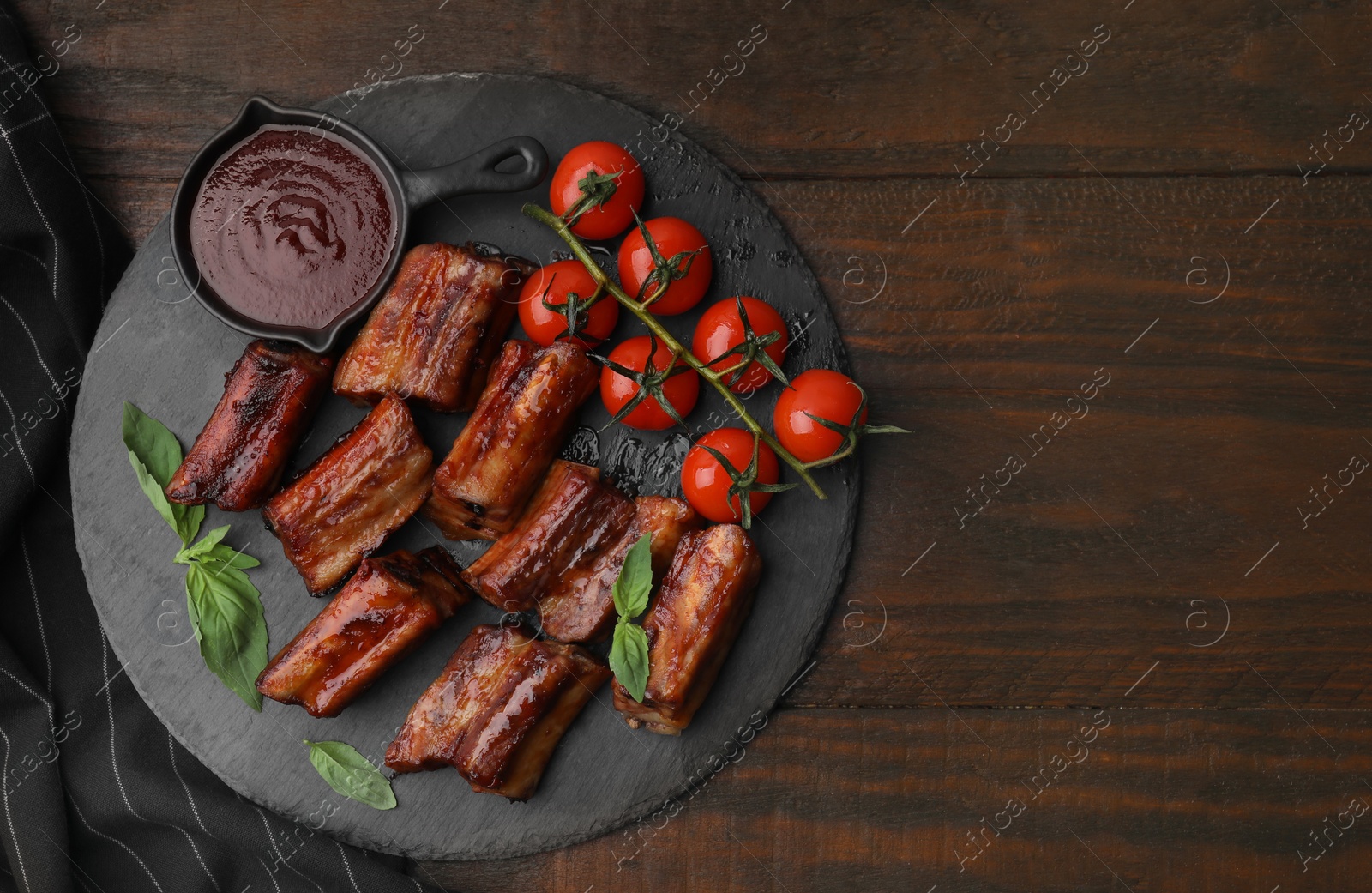 Photo of Tasty roasted pork ribs served with sauce on wooden table, top view. Space for text