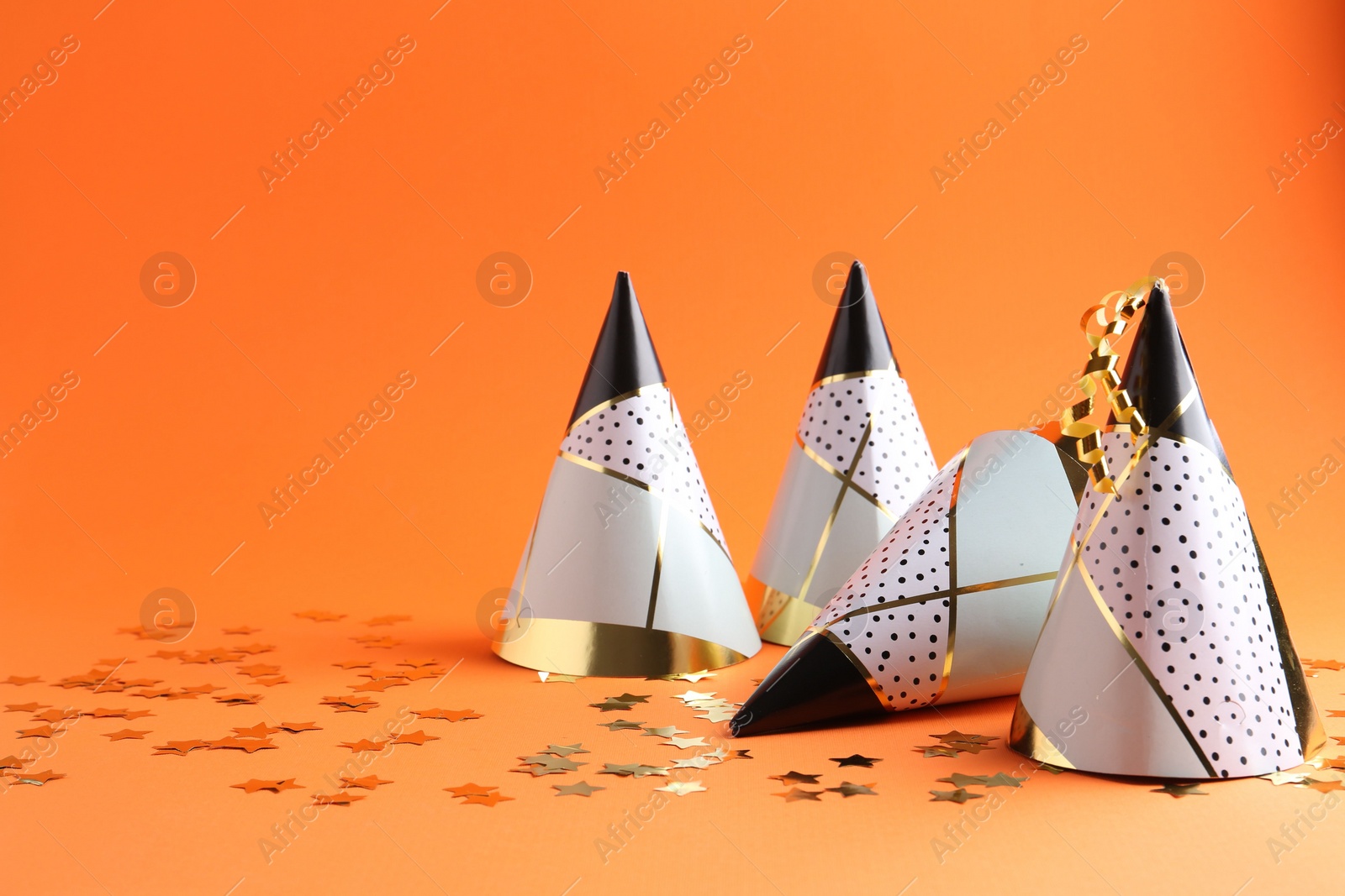Photo of Party hats and confetti on orange background, space for text