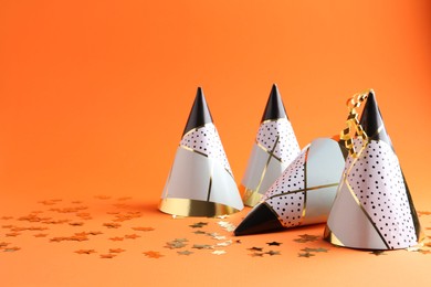 Party hats and confetti on orange background, space for text