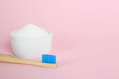 Bamboo toothbrush and bowl with baking soda on pink background. Space for text