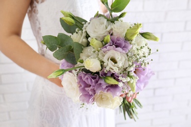 Photo of Bride holding beautiful bouquet with Eustoma flowers indoors, closeup