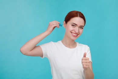 Woman using ear drops on light blue background
