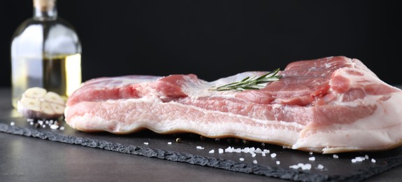 Photo of Piece of raw pork belly, rosemary and salt on grey table, closeup