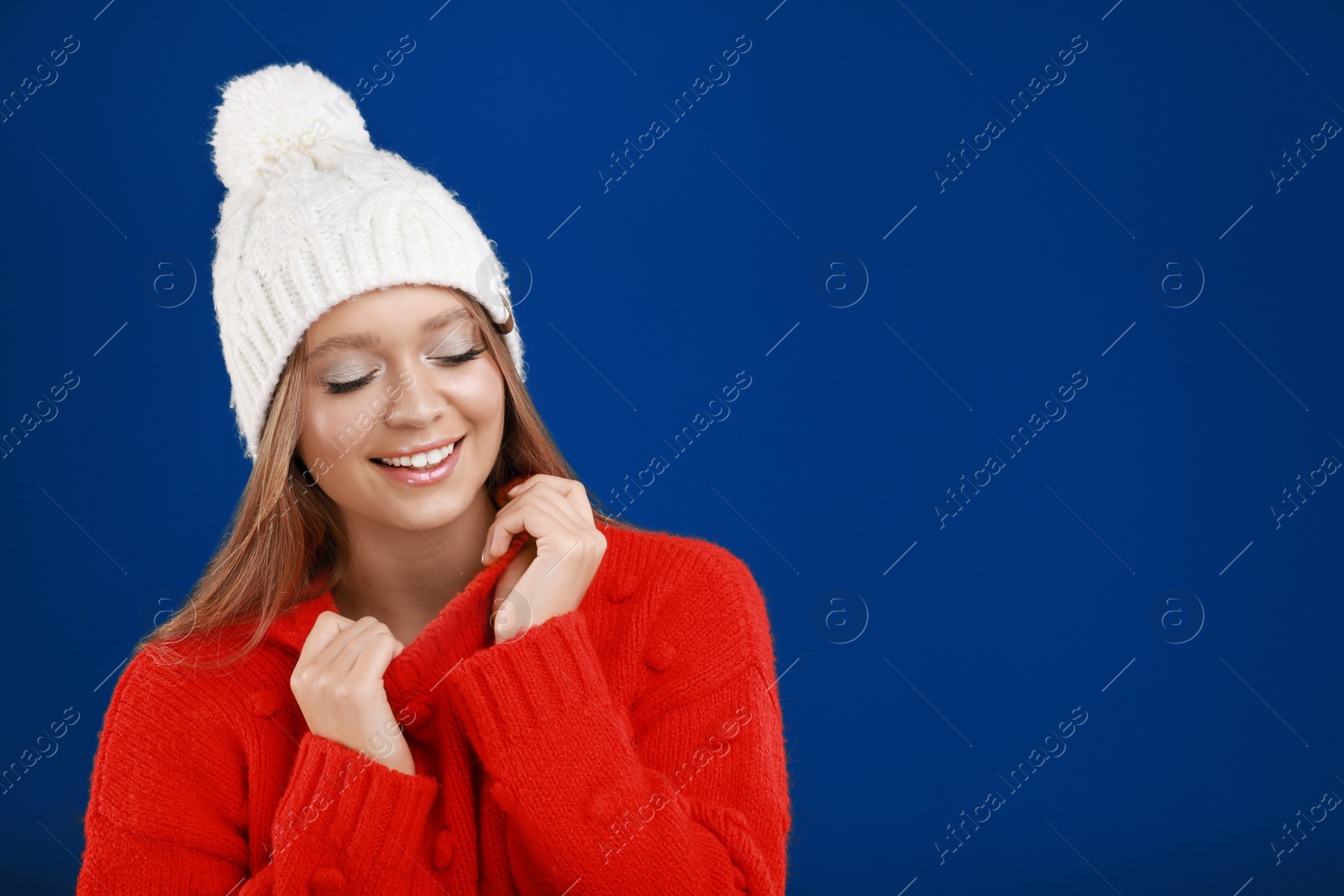 Photo of Young woman in warm sweater and hat on blue background, space for text. Winter season