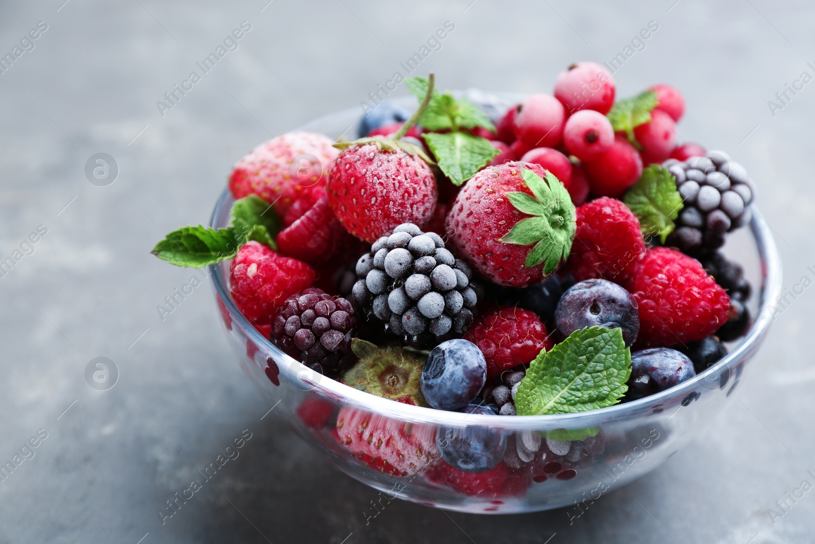 Photo of Mix of different frozen berries in bowl on grey table, closeup