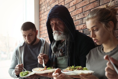 Poor people with plates of food at wall indoors