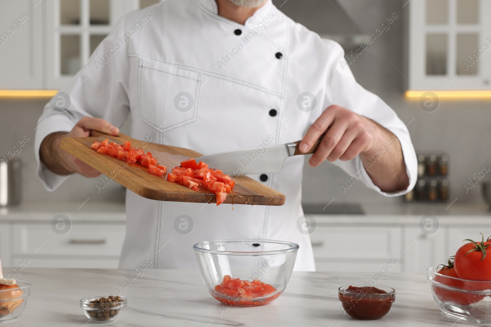 Photo of Professional chef putting cut tomatoes into bowl at white marble table indoors, closeup