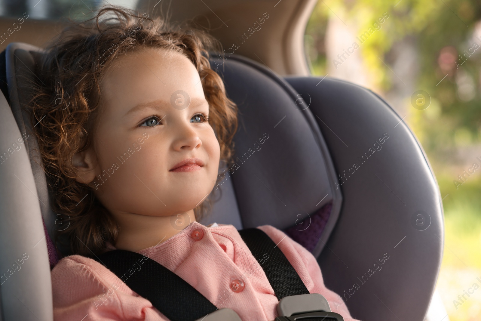 Photo of Cute little girl sitting in child safety seat inside car