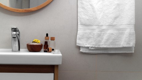 Photo of Hanging towel, sink and toiletries in bathroom. Interior design