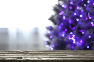 Photo of Blurred view of beautiful Christmas tree with purple lights near window indoors, focus on wooden table. Space for text