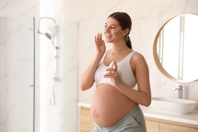 Photo of Young pregnant woman with cosmetic product in bathroom