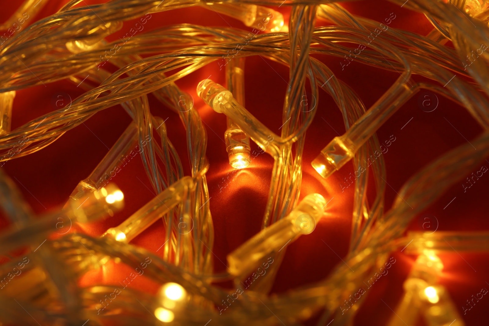 Photo of Glowing Christmas lights on red background, closeup