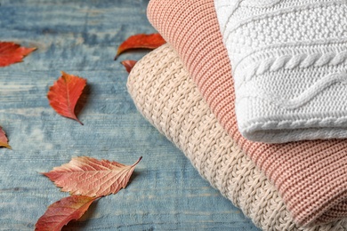 Photo of Stack of folded knitted sweaters and autumn leaves on table. Space for text