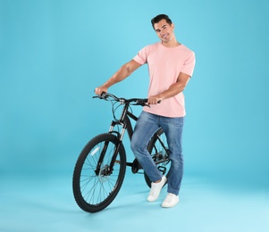 Photo of Handsome young man with modern bicycle on light blue background