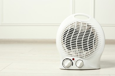 Photo of Modern electric fan heater on floor indoors, space for text