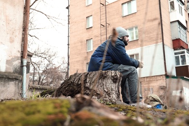 Photo of Poor homeless man sitting on stump outdoors