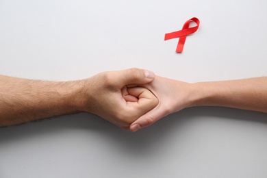 Photo of People holding hands near red awareness ribbon on white background, top view. World AIDS disease day