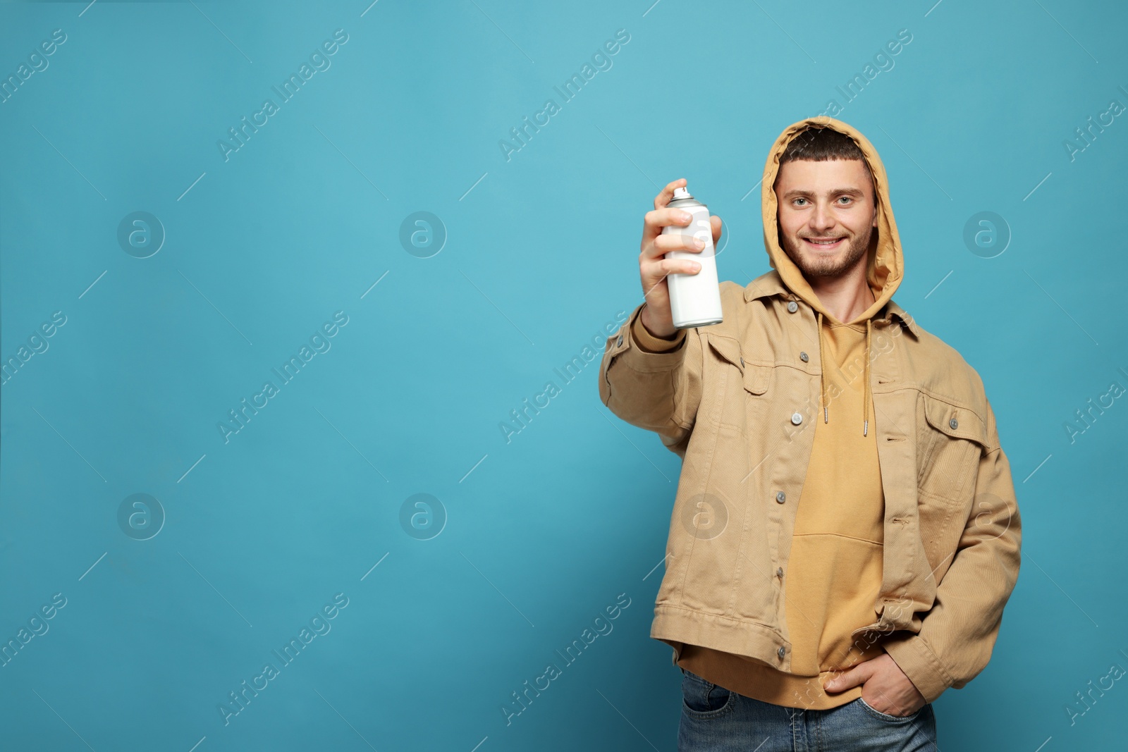 Photo of Handsome man holding white can of spray paint on light blue background. Space for text