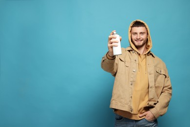 Handsome man holding white can of spray paint on light blue background. Space for text