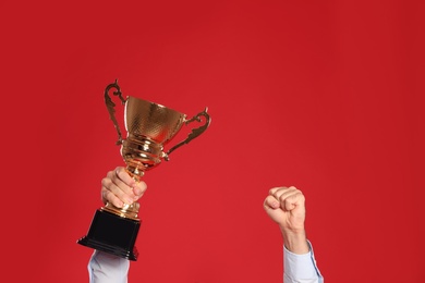 Photo of Young man with gold trophy cup on red background, closeup. Space for text