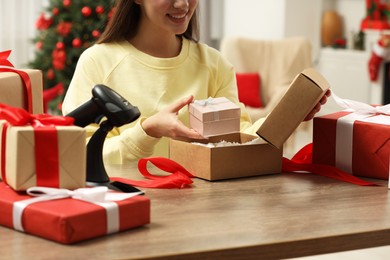 Woman putting Christmas gift box into parcel at wooden table in post office, closeup